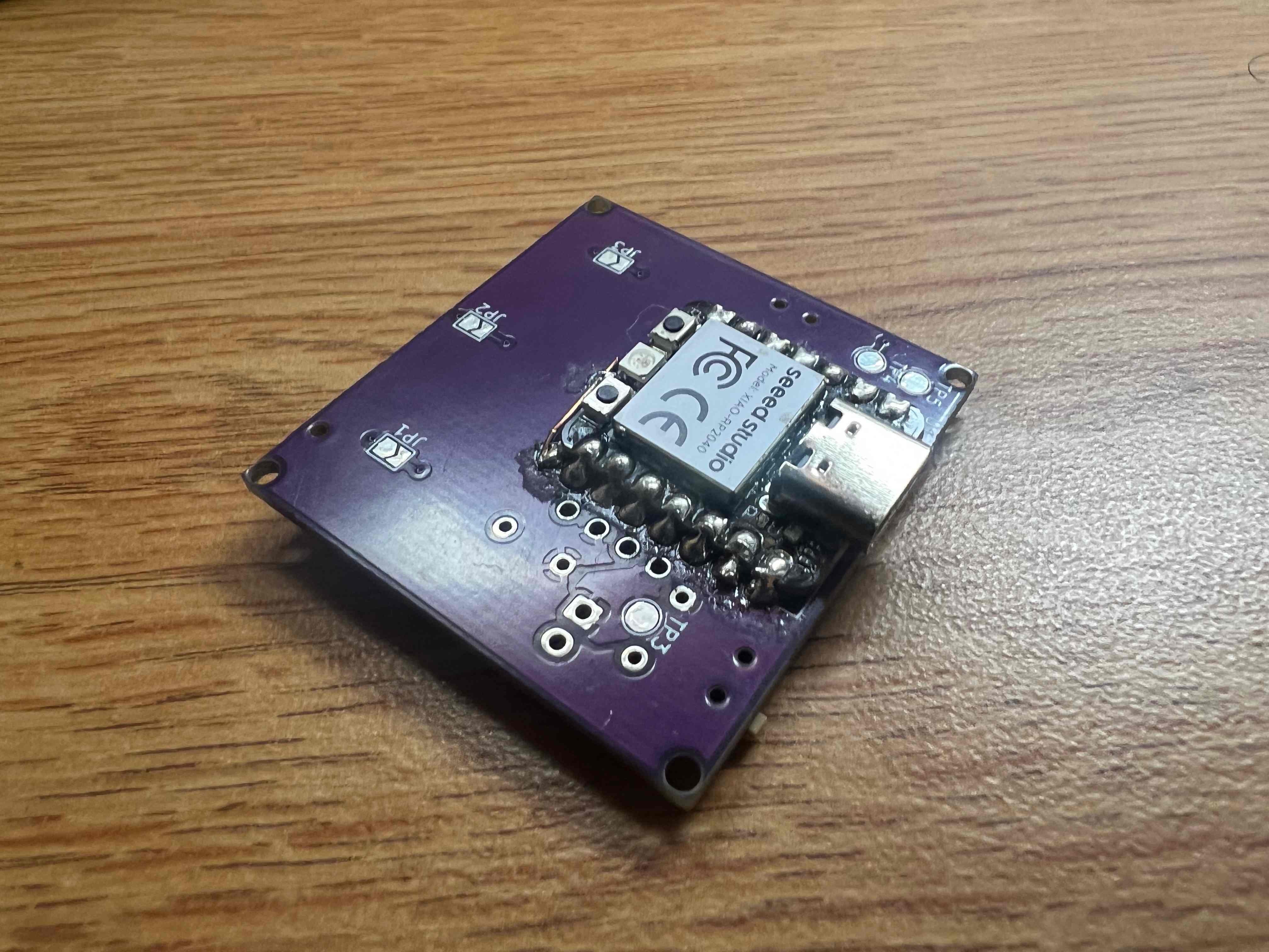 A purple square PCB with a Seeed Studio XIAO in the middle of it. Its probably about an inch and a half wide. 